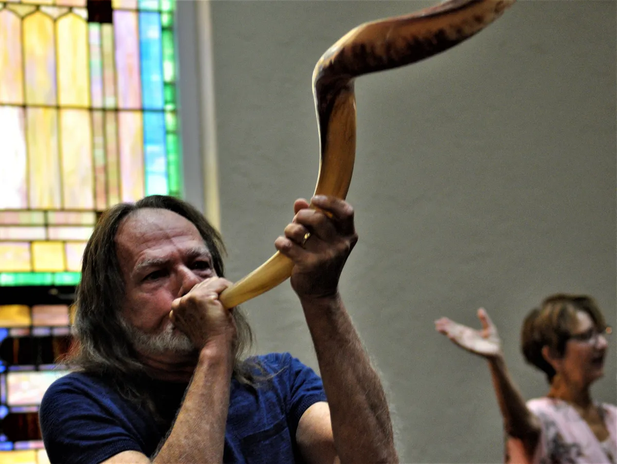 A man sounding the shofar in front of the sanctuary’s stained glass.